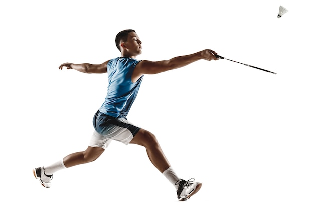 Petit garçon jouant au badminton isolé sur fond de studio blanc. Jeune mannequin en vêtements de sport et baskets avec la raquette en action, mouvement en jeu. Concept de sport, mouvement, mode de vie sain.