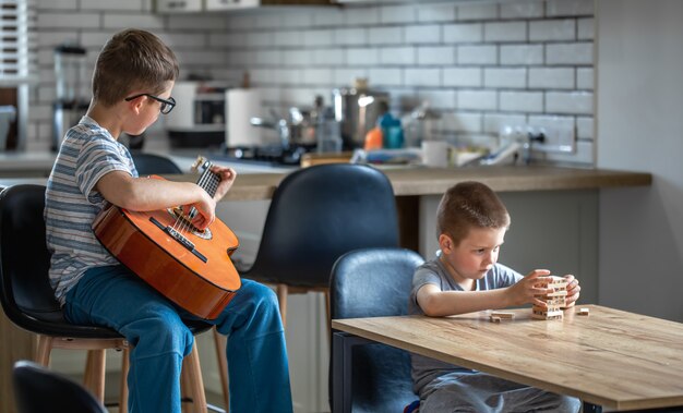 Un petit garçon joue de la guitare et son frère construit une tourelle avec des cubes en bois à la maison à table.