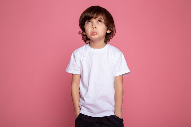 Petit garçon avec les mains dans sa poche t-shirt blanc et un jean bleu en regardant le celing sur le bureau rose