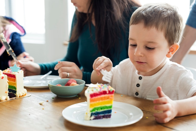 Petit garçon mangeant un gâteau de couleur arc en ciel