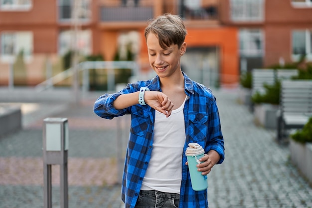 Petit garçon parlant par smartwatch bleu et buvant du thé près de l'école.