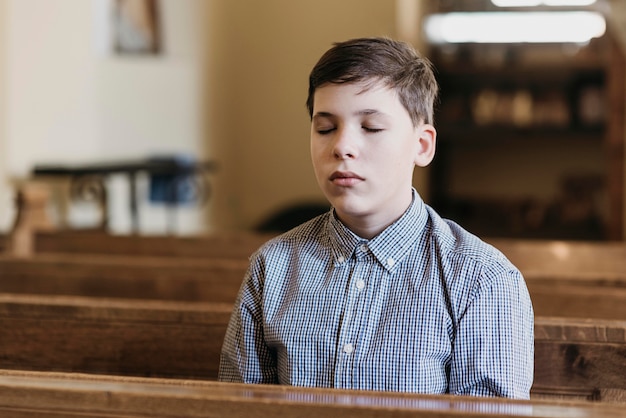 Petit garçon priant dans l'église les yeux fermés