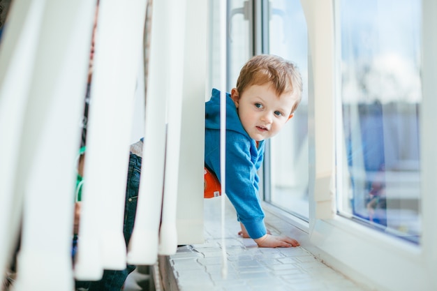 Le petit garçon se tient près du rebord de la fenêtre