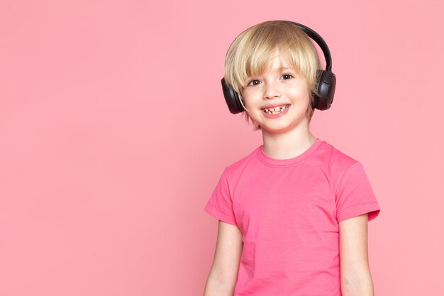 Petit garçon en t-shirt rose et un casque noir, écouter de la musique