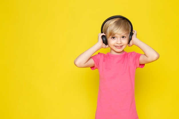 Petit garçon en t-shirt rose et un casque noir, écouter de la musique