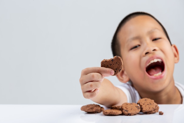 Petit garçon tient cookie voulez manger à table sur le mur blanc.