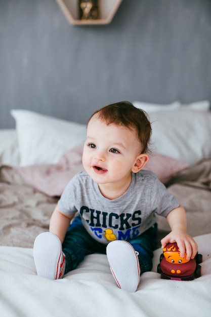 Le petit garçon avec une voiture assise sur le lit