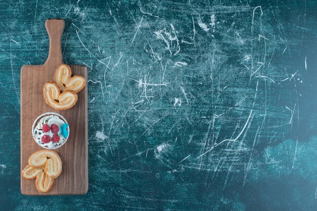 Un petit gâteau et des biscuits feuilletés regroupés sur une planche sur fond bleu. Photo de haute qualité