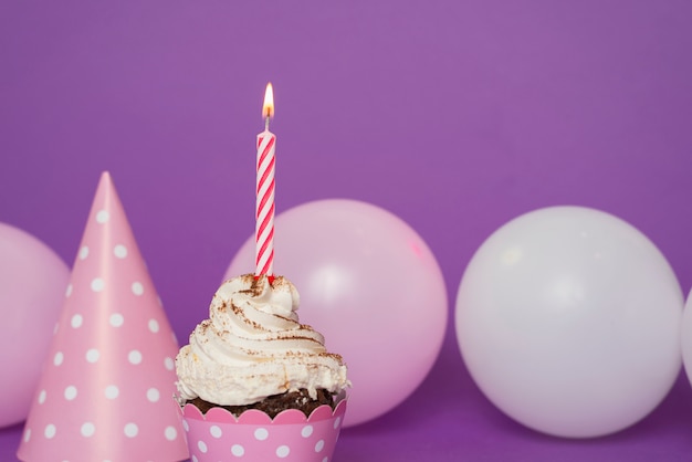 Petit gâteau avec une bougie allumée à côté du chapeau