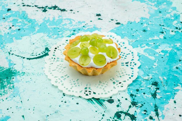 Petit gâteau à la crème délicieuse et tranches de raisins verts isolés sur bleu, gâteau sucré aux fruits au sucre cuire au four