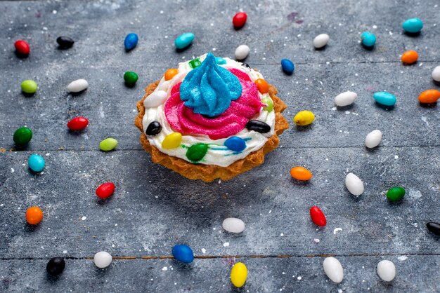 petit gâteau délicieux avec de la crème et différents bonbons colorés partout dans la lumière, bonbons gâteau de couleur sucre sucré