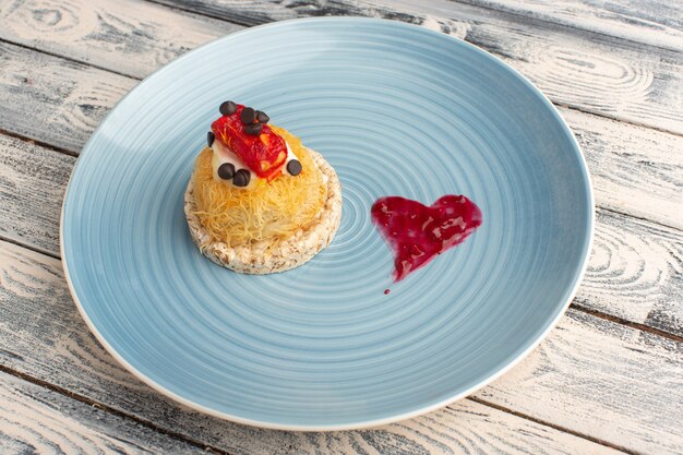 Petit gâteau délicieux avec de la crème et de la marmelade sur le dessus à l'intérieur de la plaque bleue sur fond gris