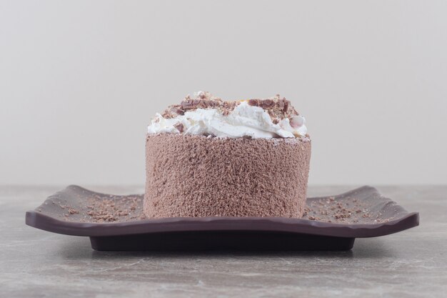 Petit gâteau avec garniture orange hachée sur un plateau sur marbre