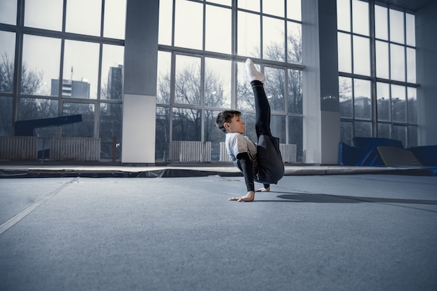 Petit gymnaste masculin s'entraînant en salle de sport, flexible et actif. Petit garçon en forme de race blanche, athlète en vêtements de sport pratiquant des exercices de force, d'équilibre. Mouvement, action, mouvement, concept dynamique.