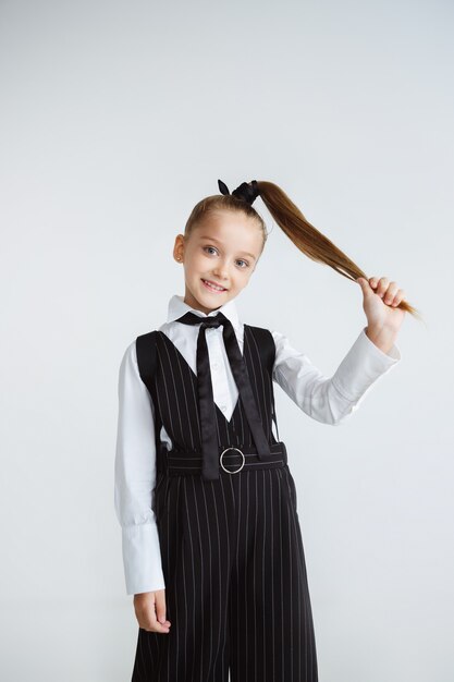 Petit modèle féminin posant en uniforme scolaire sur le mur blanc du studio