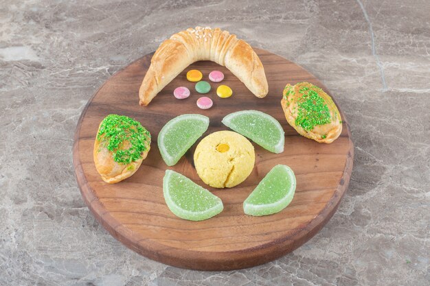 Petit pain en croissant à côté de bonbons à la gelée, d'un biscuit et de petits pains sur une planche sur une surface en marbre