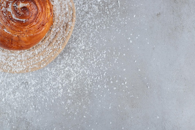 Petit pain sur un dessous de plat enduit de poudre de noix de coco sur une table en marbre.