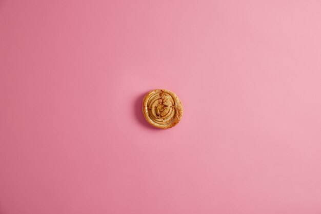 Petit pain frais en spirale cuit à la maison pour votre petit-déjeuner savoureux pour satisfaire la dent sucrée. Délicieuse pâtisserie appétissante contenant beaucoup de calories, photographiée d'en haut sur fond rose. Dessert aromatique