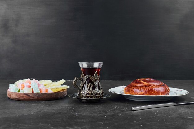 Un petit pain sucré aux fruits secs et un verre de thé sur fond noir.