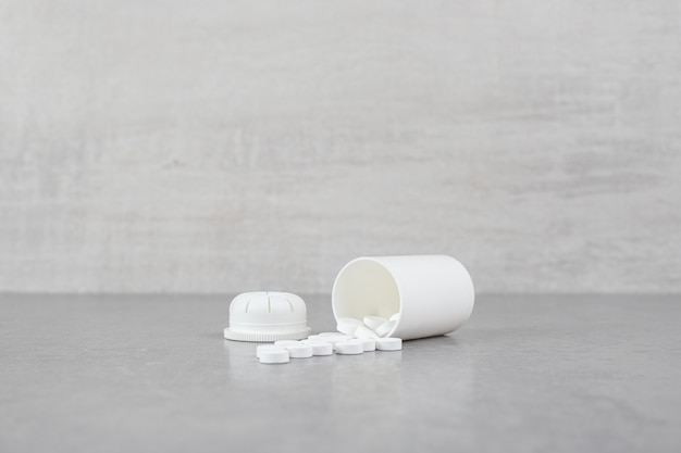 Un petit pot blanc de pilules blanches sur une surface grise