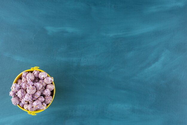 Petit seau jaune rempli de bonbons pop-corn violet sur fond bleu. photo de haute qualité