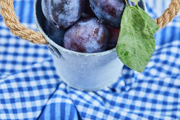 Petit seau de prunes de jardin sur une nappe bleue. Photo de haute qualité