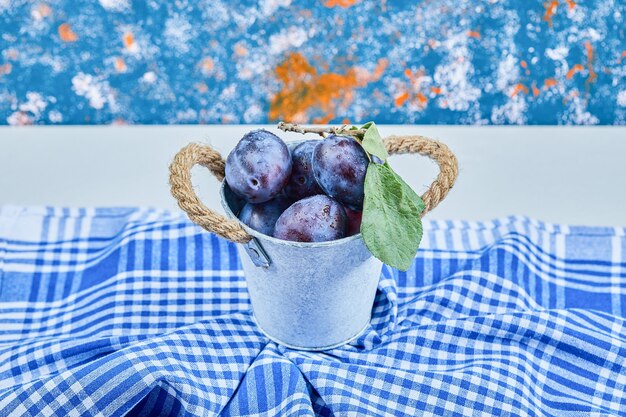 Petit seau de prunes de jardin sur une nappe bleue. Photo de haute qualité