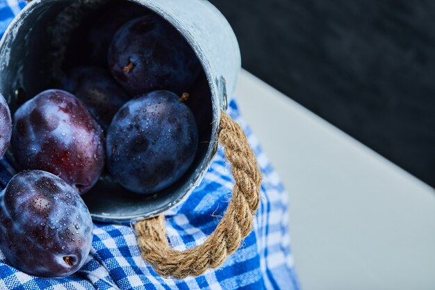 Petit seau de prunes de jardin sur noir avec nappe.