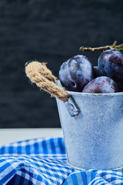 Petit seau de prunes de jardin sur noir avec nappe.