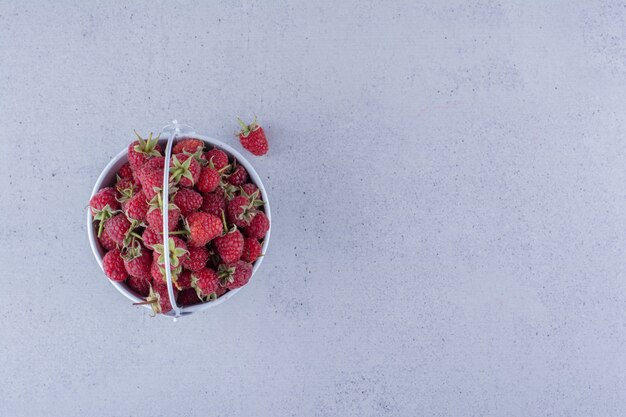 Petit seau rempli de framboises sur fond de marbre.