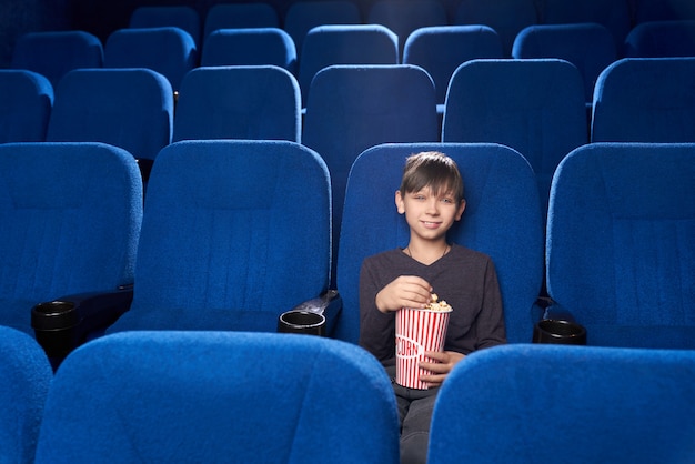 Petit spectateur masculin assis seul au cinéma et souriant