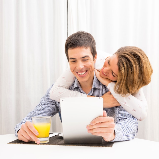 Petite amie aimant son petit ami souriant tenant un verre de jus et tablette numérique