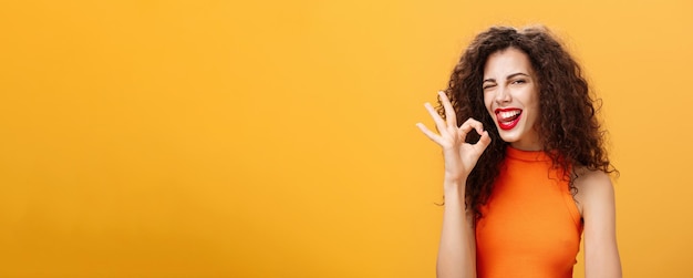 Photo gratuite petite amie caucasienne élégante et sûre d'elle avec une coiffure bouclée clignant de l'œil joyeusement et qui sort de la tong