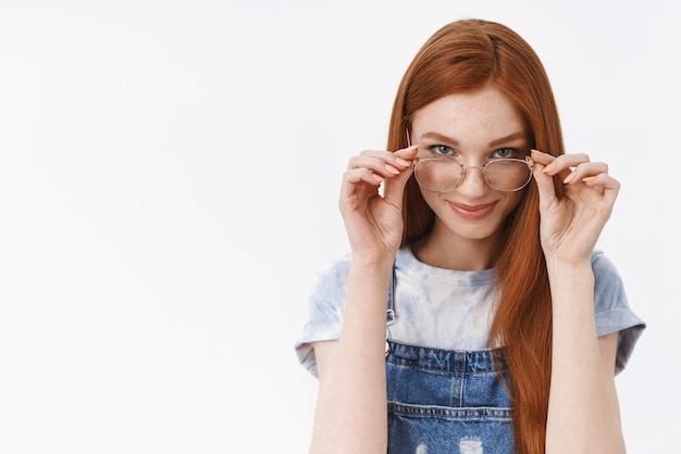 Petite amie impertinente rousse belle rusée mettre des lunettes regarder sous le front sournois heureux avoir quelque chose de curieux à l'esprit sourire ravi se tenir debout fond blanc affirmé