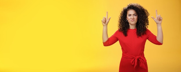 Photo gratuite petite amie de mauvaise humeur peu impressionnée mécontente avec une coiffure bouclée en robe élégante rouge levant les mains poin