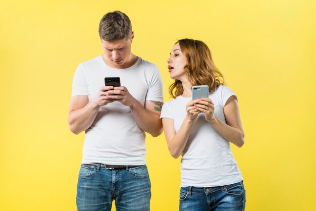 Petite amie suspecte espionnant son petit ami texto sur téléphone portable dans un contexte jaune