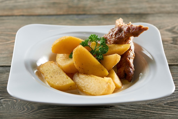 Petite assiette de restaurant blanche servie avec des tranches de pommes de terre frites dorées, une saucisse fine et décorée de feuilles de persil. Semble très délicieux et nourrissant.