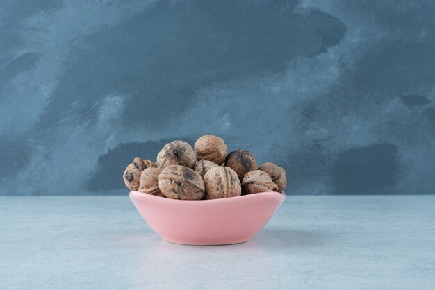 Une petite assiette rose pleine de noix sur fond de marbre. Photo de haute qualité