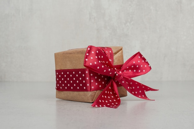 Une petite boîte cadeau avec un arc rouge sur un mur blanc.