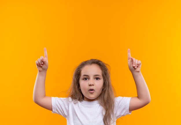 Petite écolière portant un t-shirt blanc a mis son doigt sur un mur orange isolé