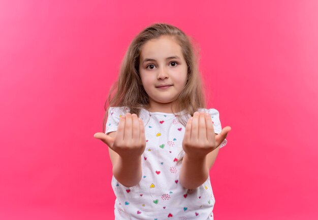 Petite écolière portant un t-shirt blanc montrant la taille sur un mur rose isolé