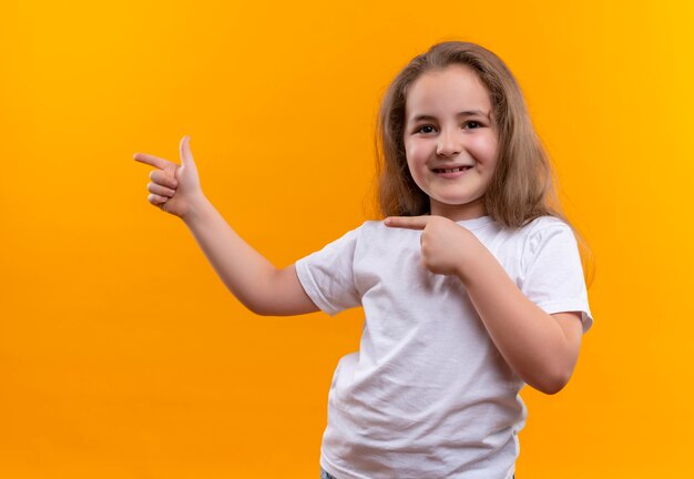 Petite écolière portant un t-shirt blanc pointe vers le côté sur un mur orange isolé