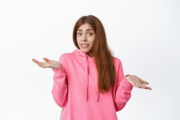 Petite erreur oups Jolie fille haussant les épaules et ayant l'air coupable dire désolé je ne sais pas comprendre quelque chose debout indécis sur fond blanc