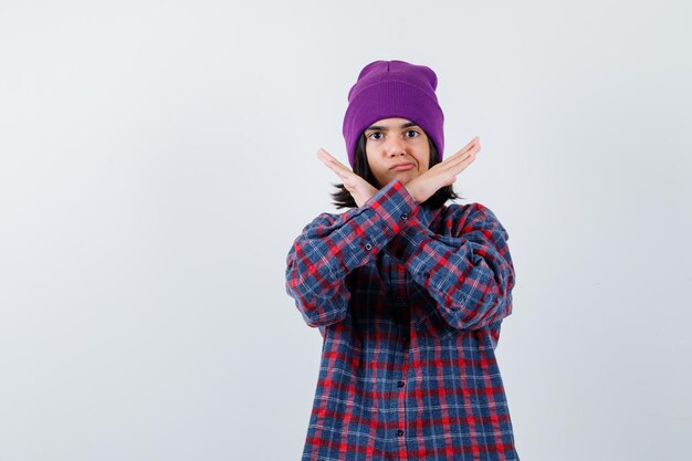 Petite femme en chemise à carreaux et bonnet montrant un geste d'arrêt à la recherche de sérieux