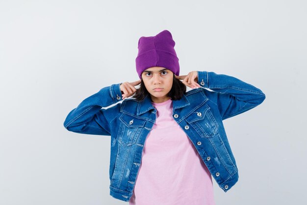 Petite femme se branchant les oreilles avec les doigts dans une veste en jean t-shirt à l'air ennuyé