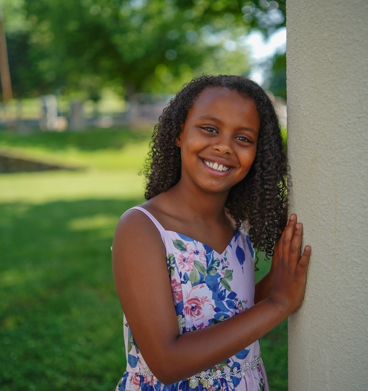 Photo gratuit petite fille afro-américaine souriante dans un jardin entouré de verdure sous la lumière du soleil
