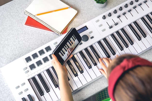 Photo gratuite une petite fille apprend à jouer du piano avec un cours de musique en ligne sur smartphone