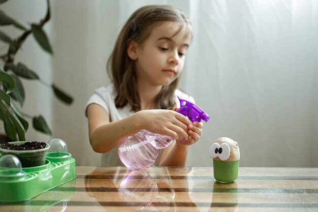 Une petite fille asperge d'eau la tête du jouet avec laquelle pousse l'herbe.