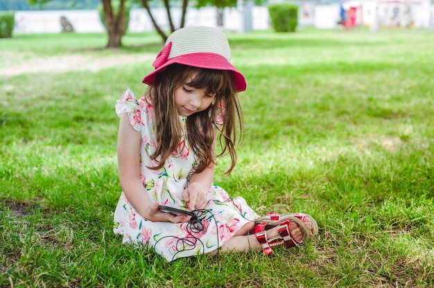 Petite fille assise sur l&#39;herbe en regardant un mobile avec un casque