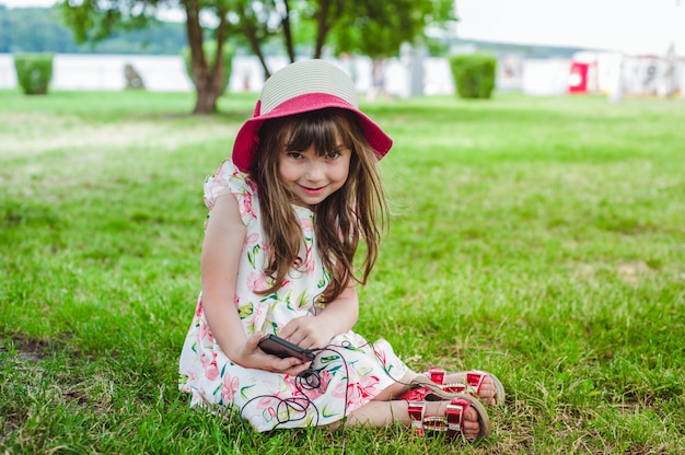 Photo gratuite petite fille assise sur l'herbe en regardant un mobile avec un casque